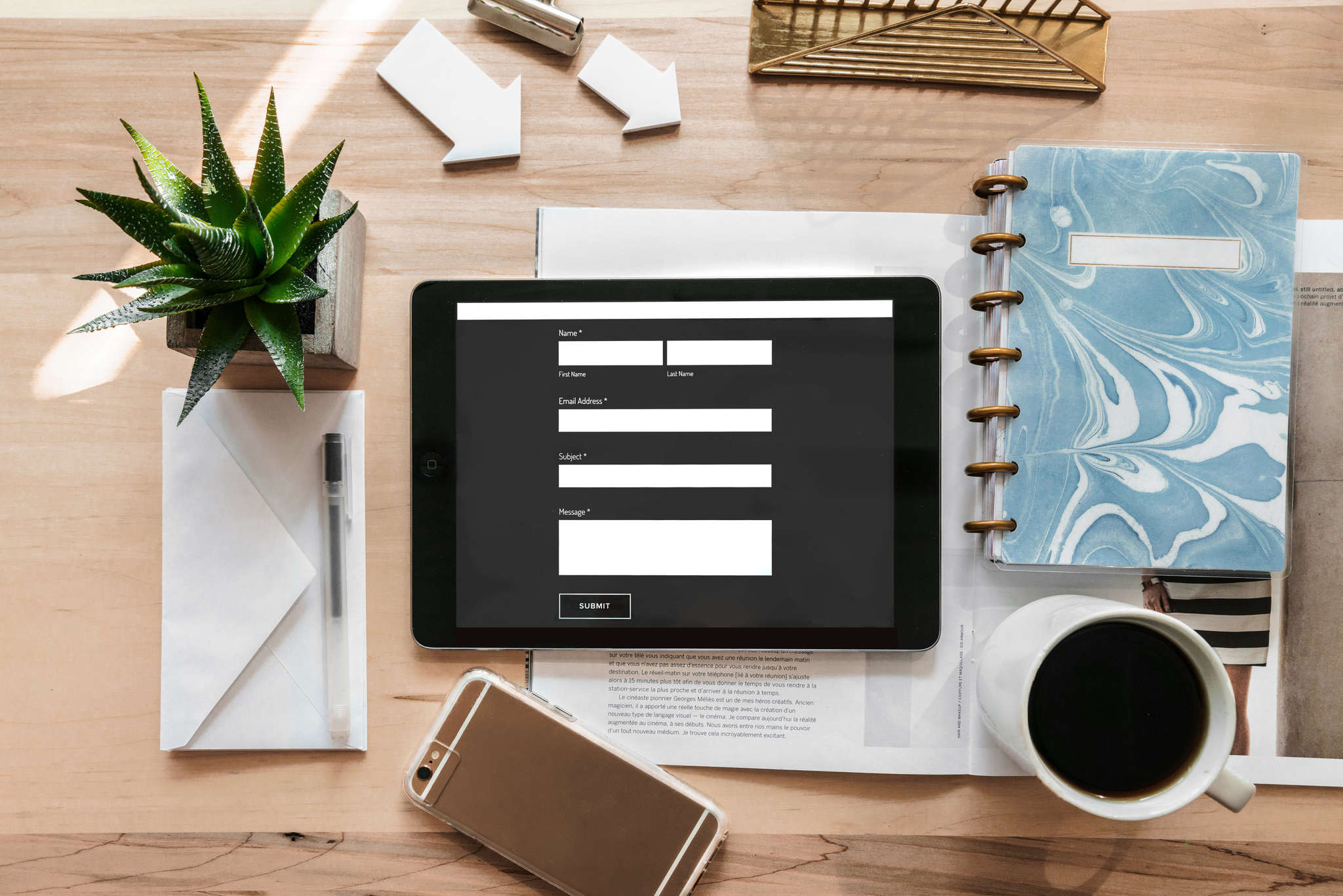 contact form on a tablet laid out in a office, along with a plant, notebook, coffee and mobile phone