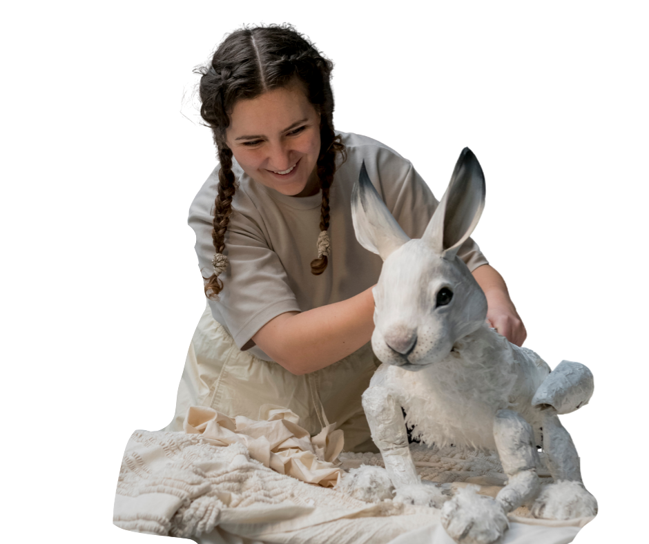 a brown-skinned young woman puppeteers the head of a polar bear puppet. She is wearing a face mask.