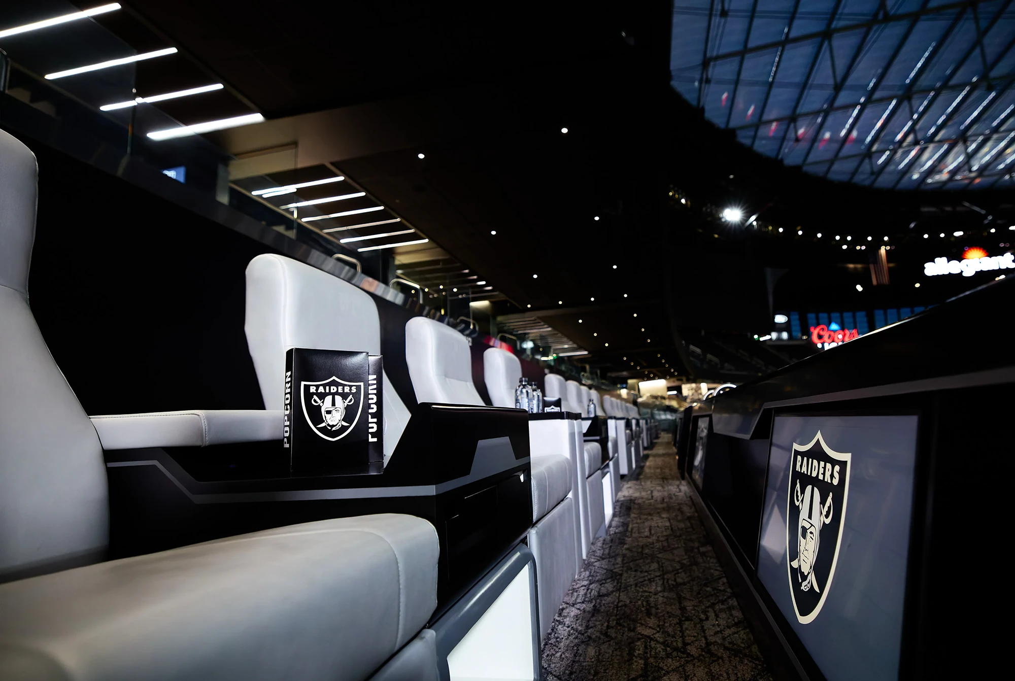 Fans seated in a luxury suite at Allegiant Stadium watching a football game, some wearing Raiders apparel.