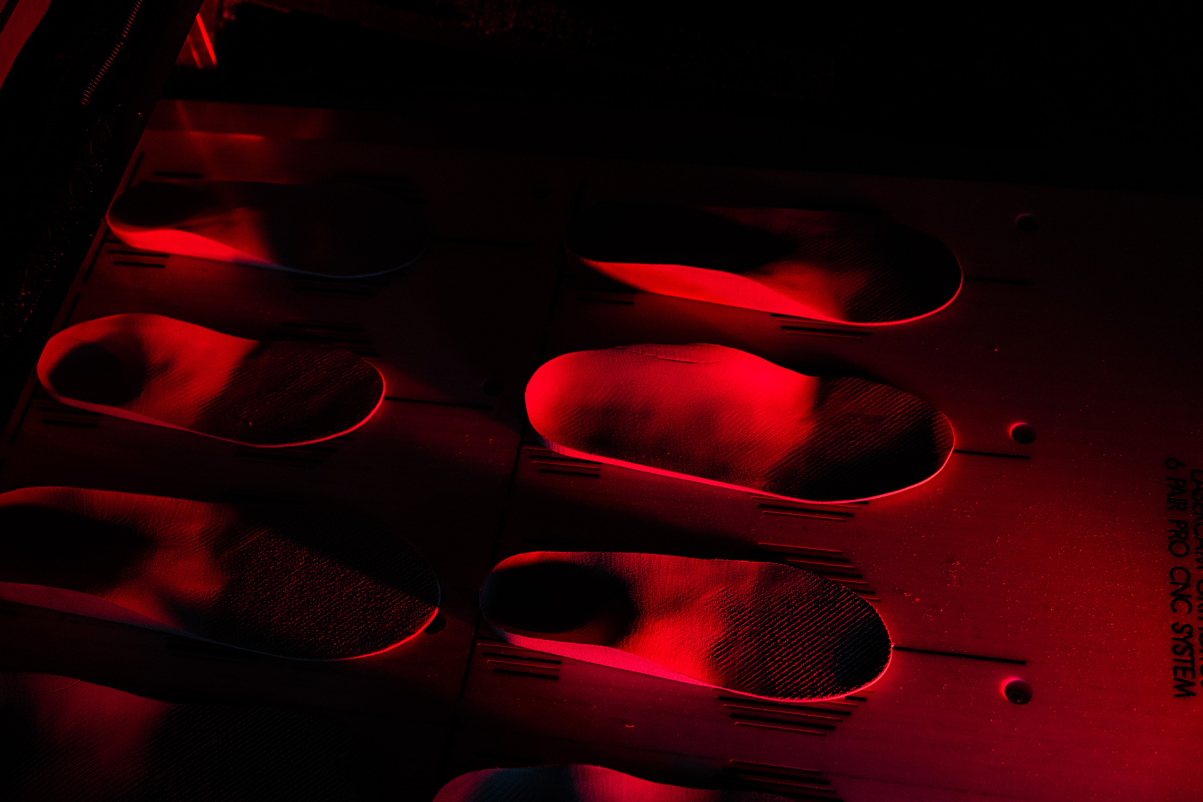 Several orthotic insoles arranged in pairs on a surface illuminated by red light.