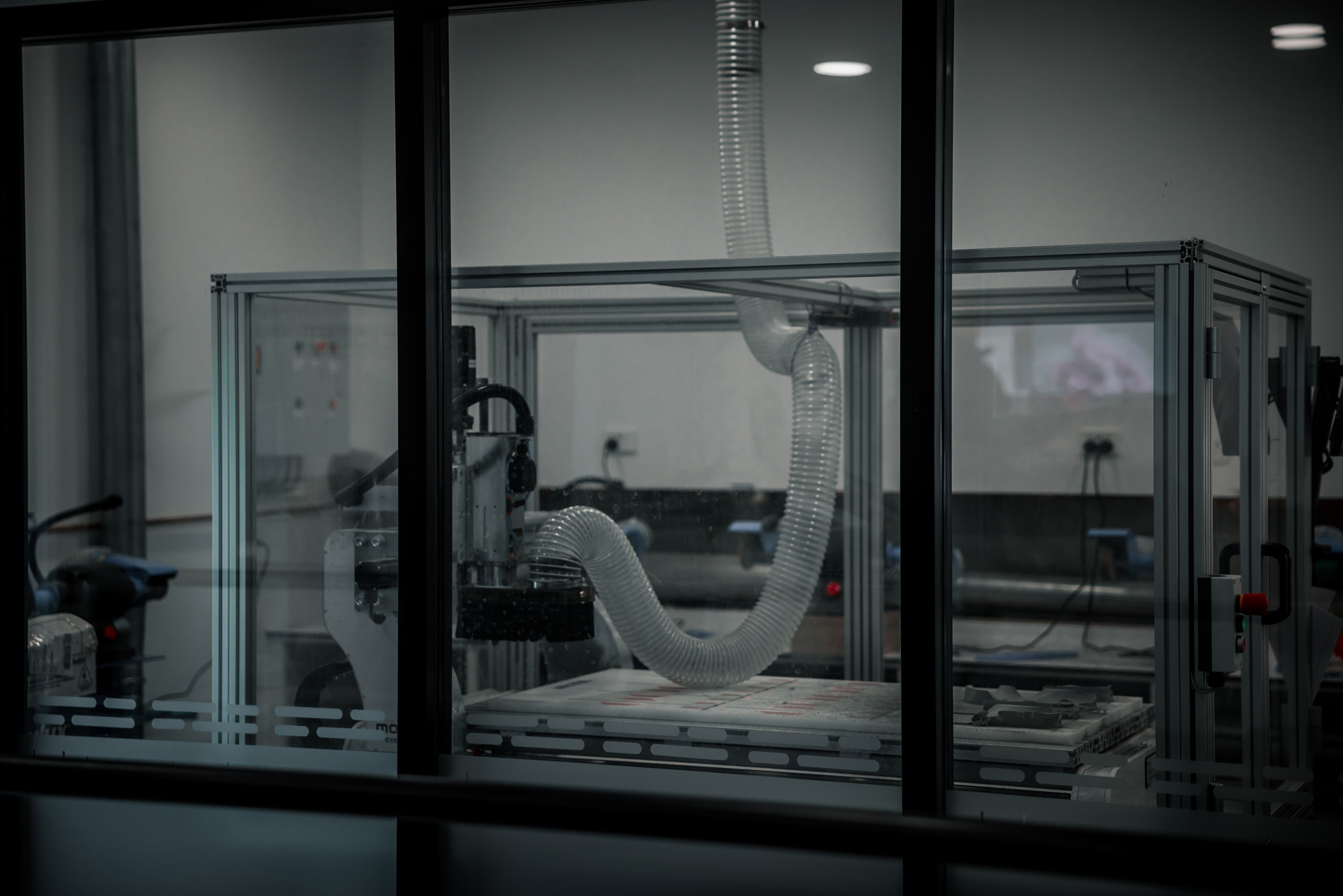 Industrial machine enclosed in glass with flexible exhaust tubing inside a laboratory or workshop.