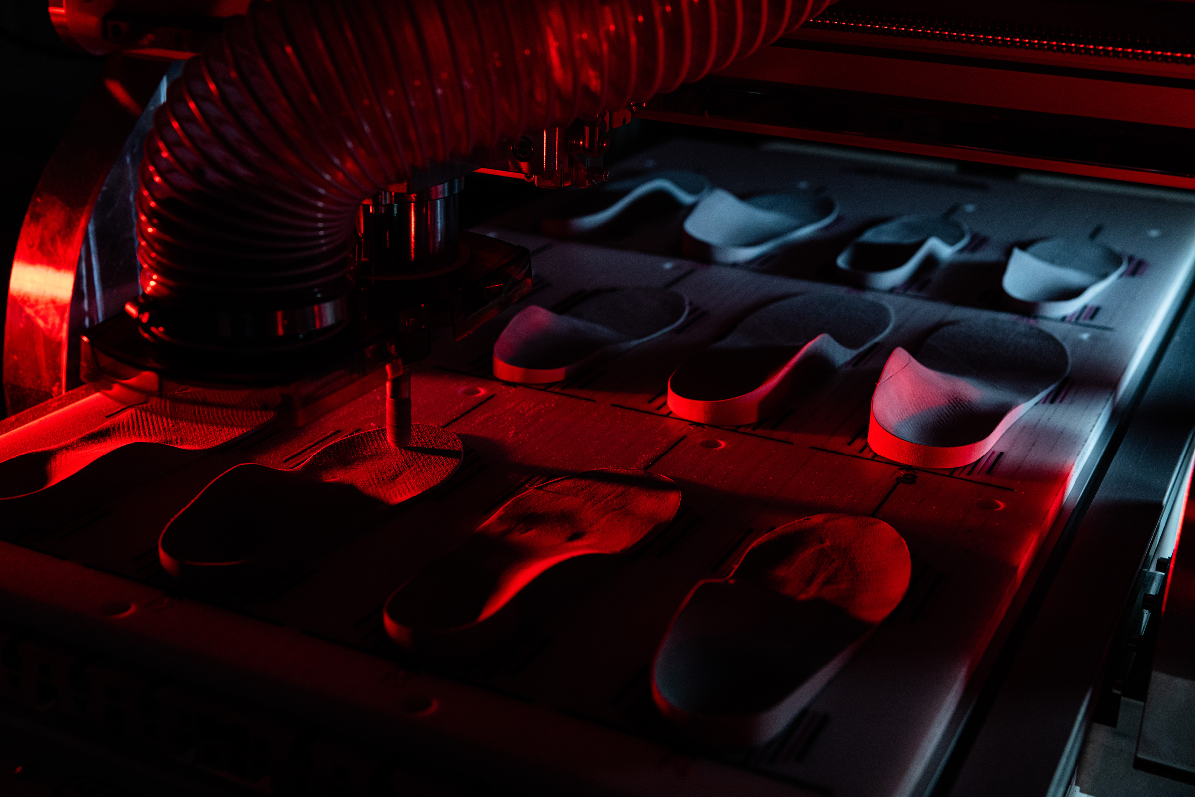 Machine shaping multiple shoe insoles on a production line under red lighting.
