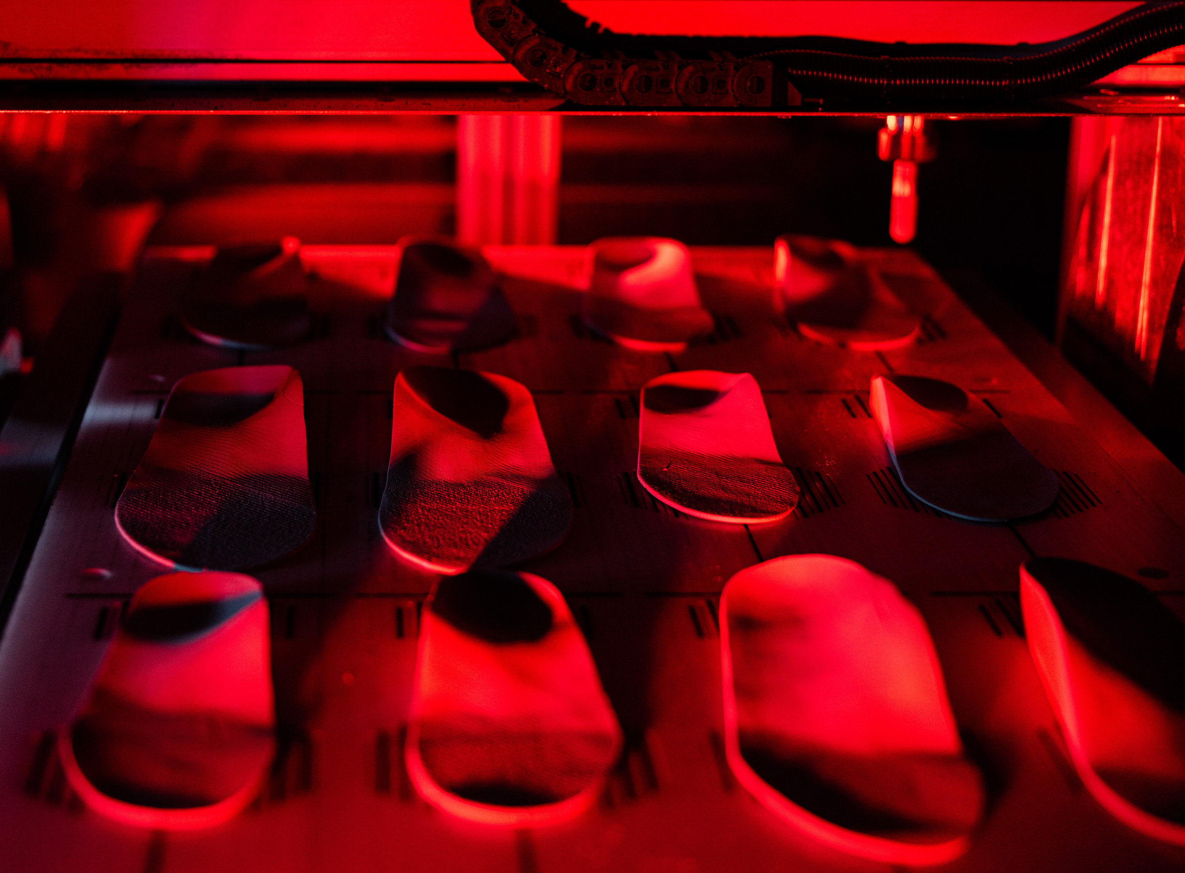 Rows of shoe insoles on a conveyor belt inside a machine under red lighting.