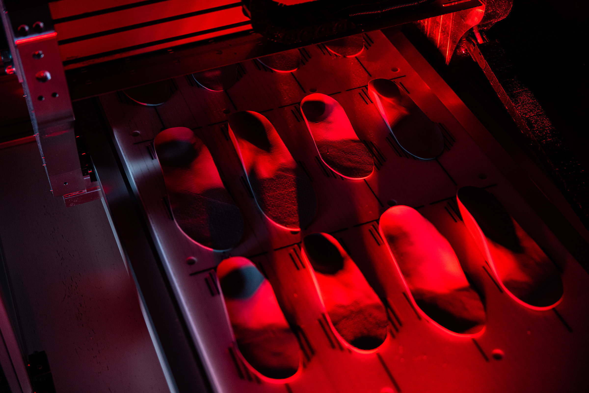 Industrial machine with red lighting molding shoe insoles in aligned cavities.