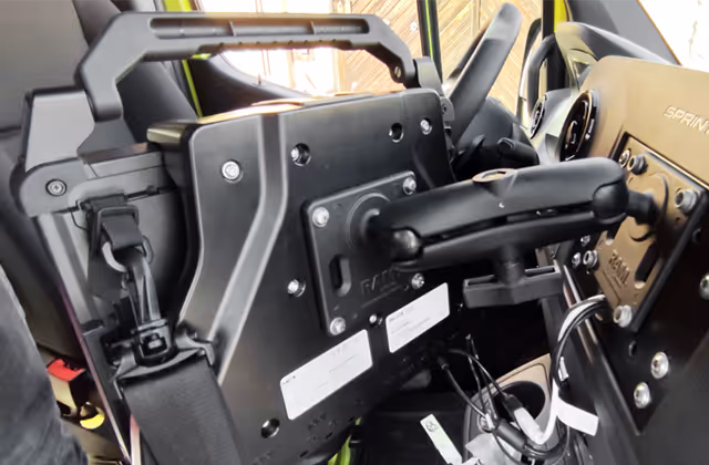 Close-up of a mounted tablet holder attached to a vehicle dashboard, with visible straps and adjustment mechanisms.