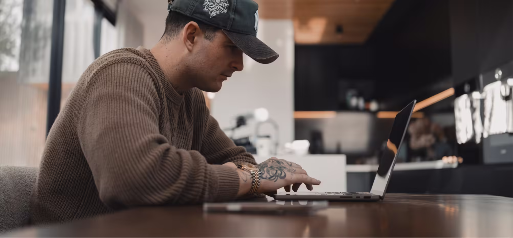 a man wearing a hat and a brown sweater using a laptop