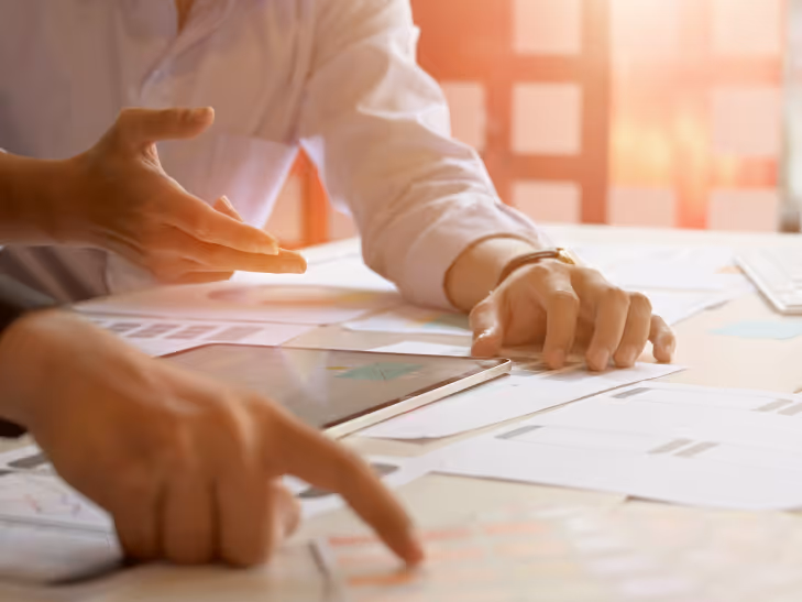 Deux personnes en chemise blanche collaborant sur des documents et une tablette lors d'une réunion de travail au bureau.