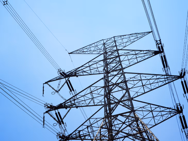 Vue en contre-plongée d'un pylône électrique en acier avec des câbles haute tension sur un ciel bleu clair.