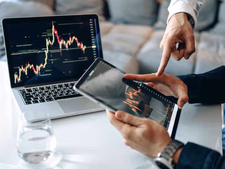 Personnes examinant des graphiques financiers sur une tablette et un ordinateur portable dans un bureau.
