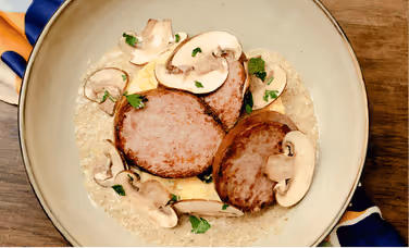 Assiette avec deux tranches de viande, champignons tranchés et garniture verte sur un lit de riz.