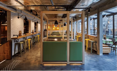 Intérieur moderne d'un café avec des sièges verts séparés par des cloisons en bois, grandes fenêtres à droite et tabourets métalliques le long du comptoir.