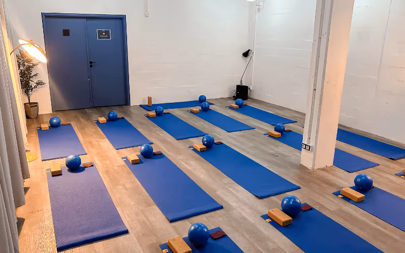 Salle de yoga avec tapis bleus alignés sur un sol en bois, chaque tapis avec un ballon bleu, deux blocs et une sangle.