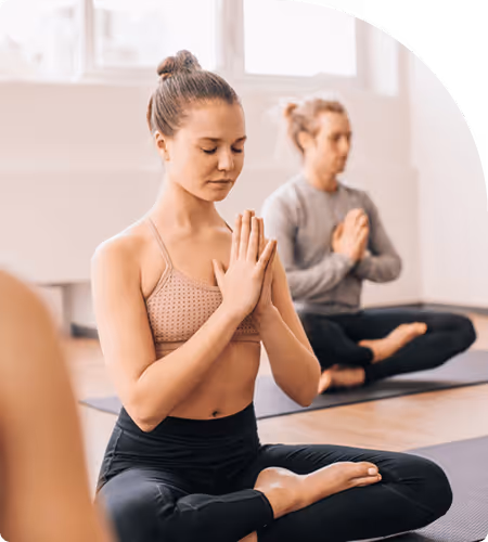Deux personnes en position assise de méditation pratiquent le yoga dans un studio lumineux.