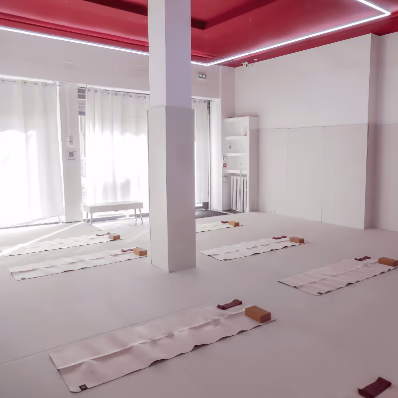 Salle de yoga lumineuse avec tapis blancs disposés au sol, briques de yoga et sangle à chaque place, plafond rouge avec éclairage LED.