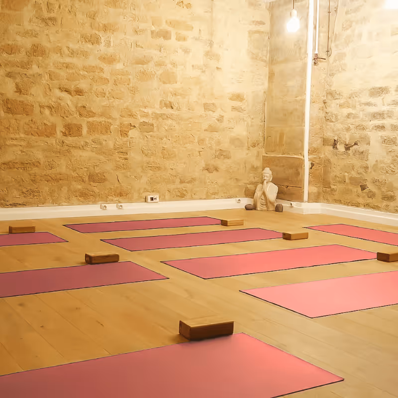Salle de yoga avec tapis roses et briques apparentes, statue de Bouddha en arrière-plan.