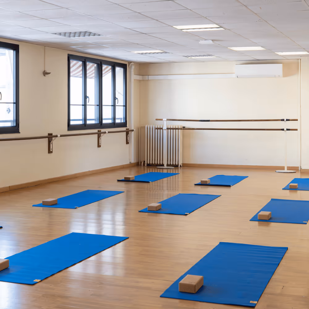 Salle de yoga avec tapis bleus et blocs de yoga disposés sur un sol en bois clair.