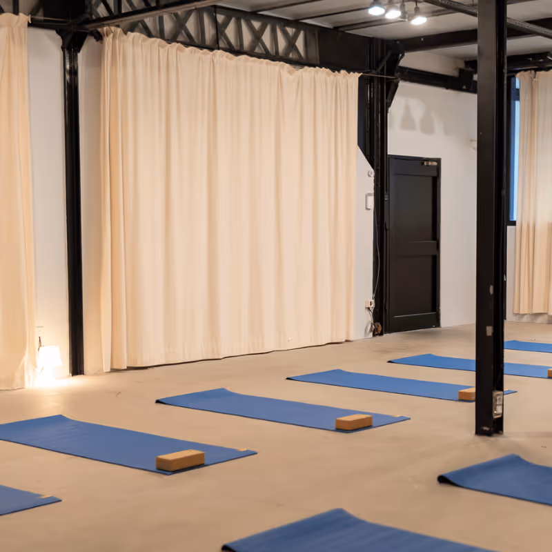 Salle de yoga avec des tapis bleus et des briques de yoga disposés sur un sol en bois, grands miroirs au mur