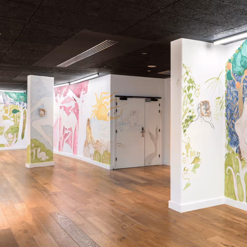 Intérieur lumineux avec parquet et murs blancs ornés de grandes peintures murales colorées.