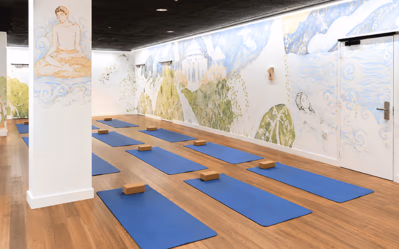 Salle de yoga avec tapis bleus alignés et murs décorés de fresques apaisantes au style asiatique.