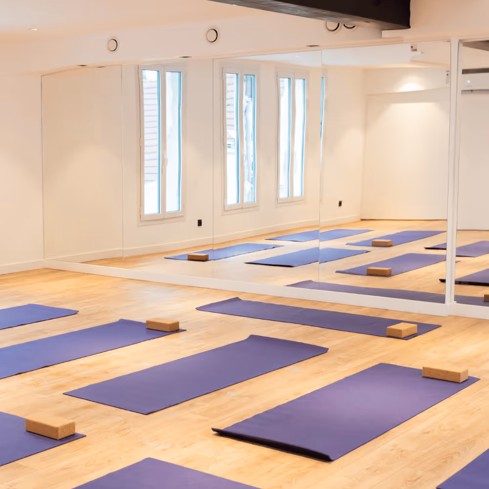 Salle lumineuse avec tapis de yoga et blocs en bois disposés sur un sol en bois clair.