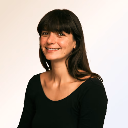 Portrait d'une femme souriante aux cheveux bruns longs et franges, portant un haut noir.