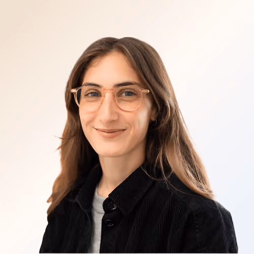 Portrait d'une femme avec des lunettes et un manteau noir, souriant légèrement sur fond clair.