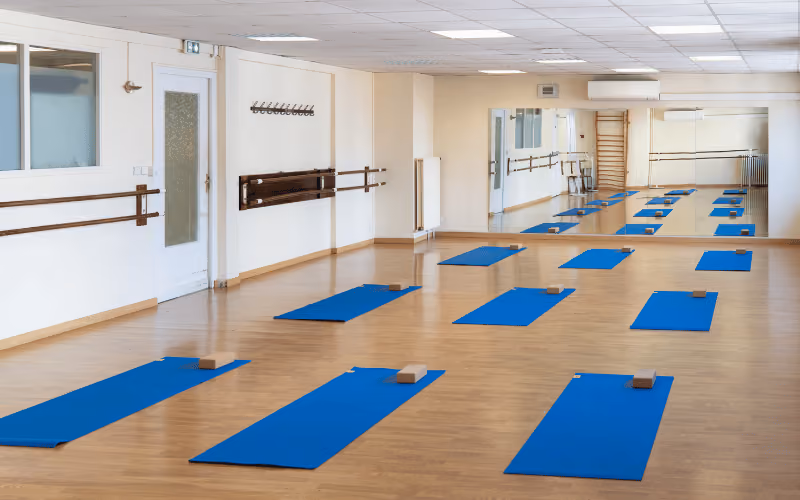 Salle du studio Yoze Pyramides avec tapis bleus, blocs de yoga, barres murales et grands miroirs.