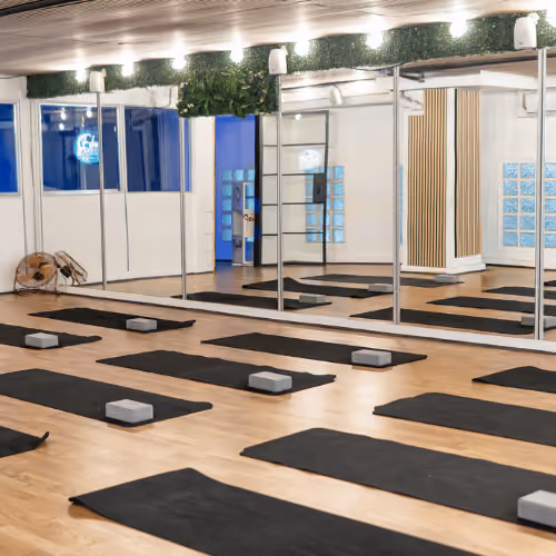 Salle de yoga avec des tapis bleus et des briques de yoga disposés sur un sol en bois, grands miroirs au mur