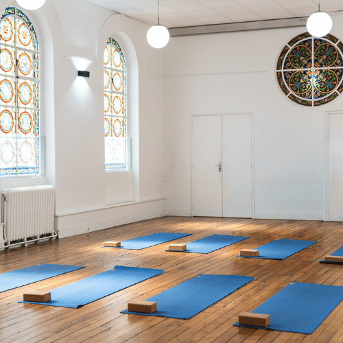 Salle de yoga avec des tapis bleus et des briques de yoga disposés sur un sol en bois, grands miroirs au mur
