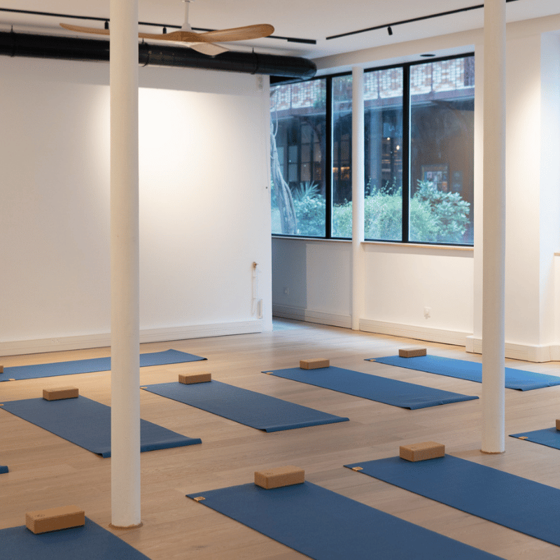 Vue du studio Charonne – Atelier 77 avec tapis bleus, briques et grandes fenêtres