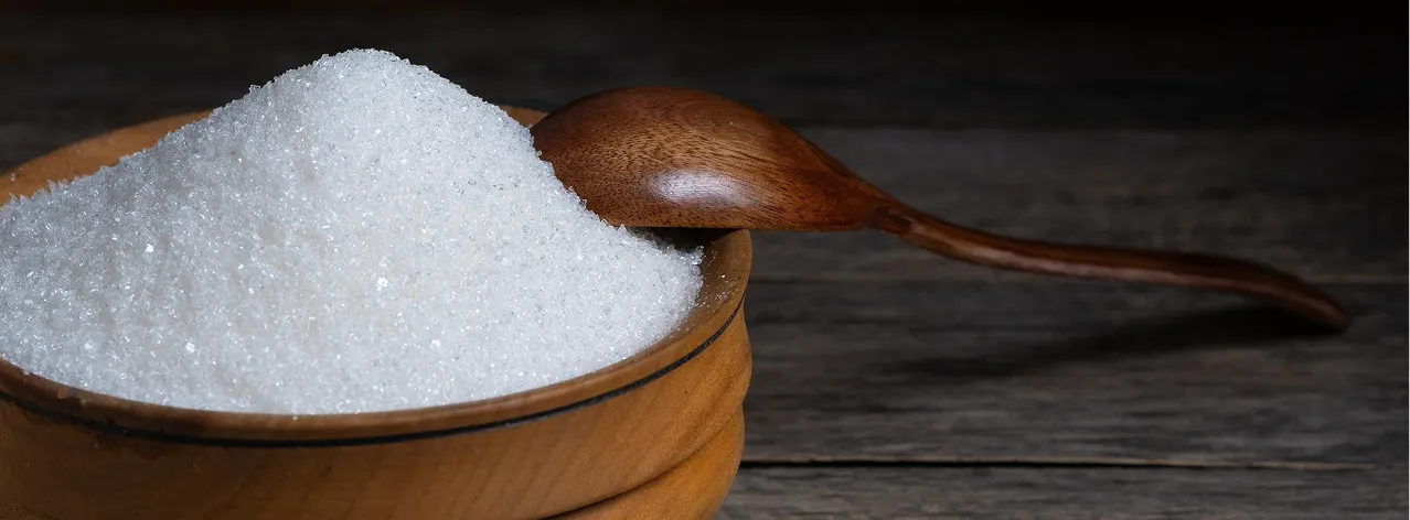 Close-up of a wooden bowl filled with granulated white sugar and a wooden spoon resting on top.