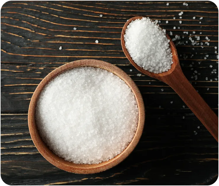Wooden bowl and spoon filled with sugar on a dark wooden surface.
