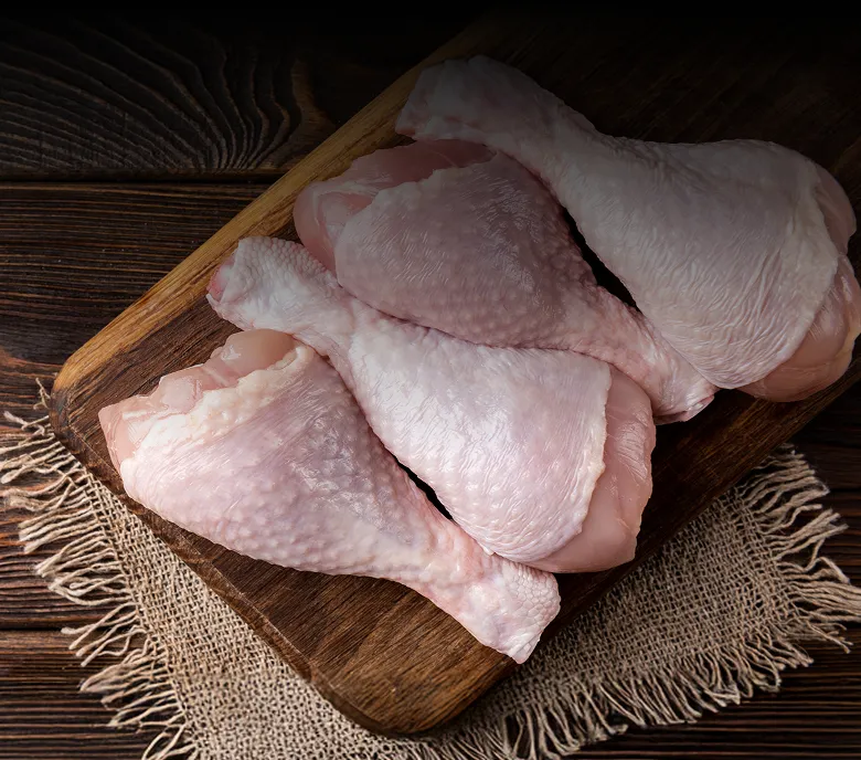 Four raw Armin Plus chicken drumsticks with skin on a wooden cutting board over a burlap cloth on a dark wood surface.