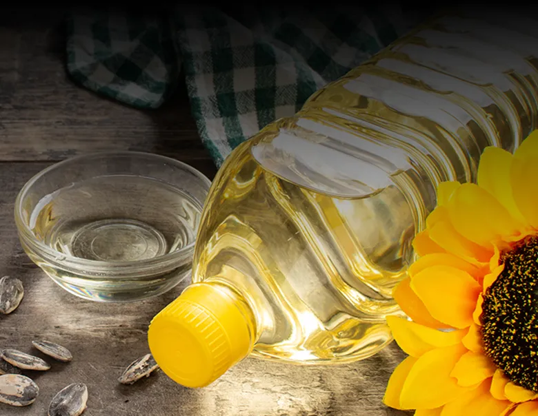Clear plastic bottle with yellow cap filled with Armin Plus sunflower oil, a glass bowl of oil, a sunflower, and a few sunflower seeds on a wooden surface.