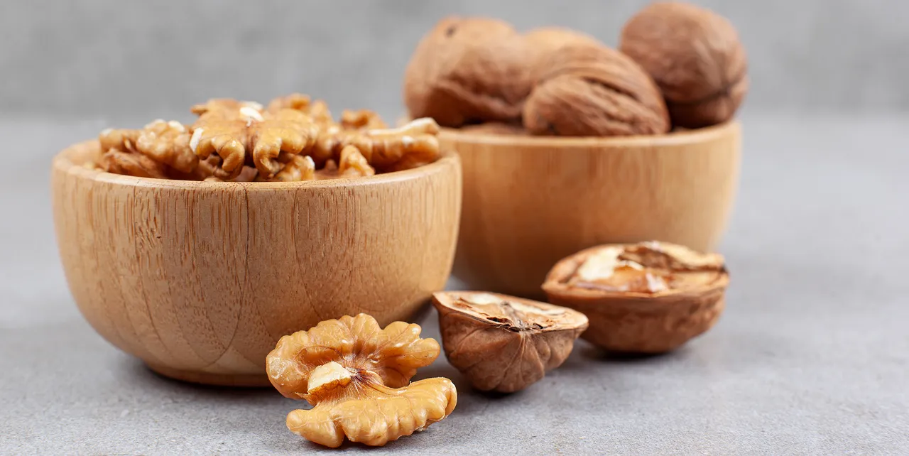 Shelled and unshelled Armin Plus walnuts in wooden bowls on a gray surface with some walnut halves in front.