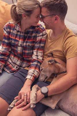 Couple cuddles on the couch with their dog