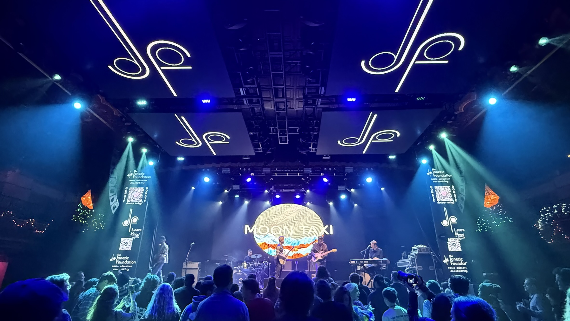 A concert from the audience view with a person making a heart with their hands