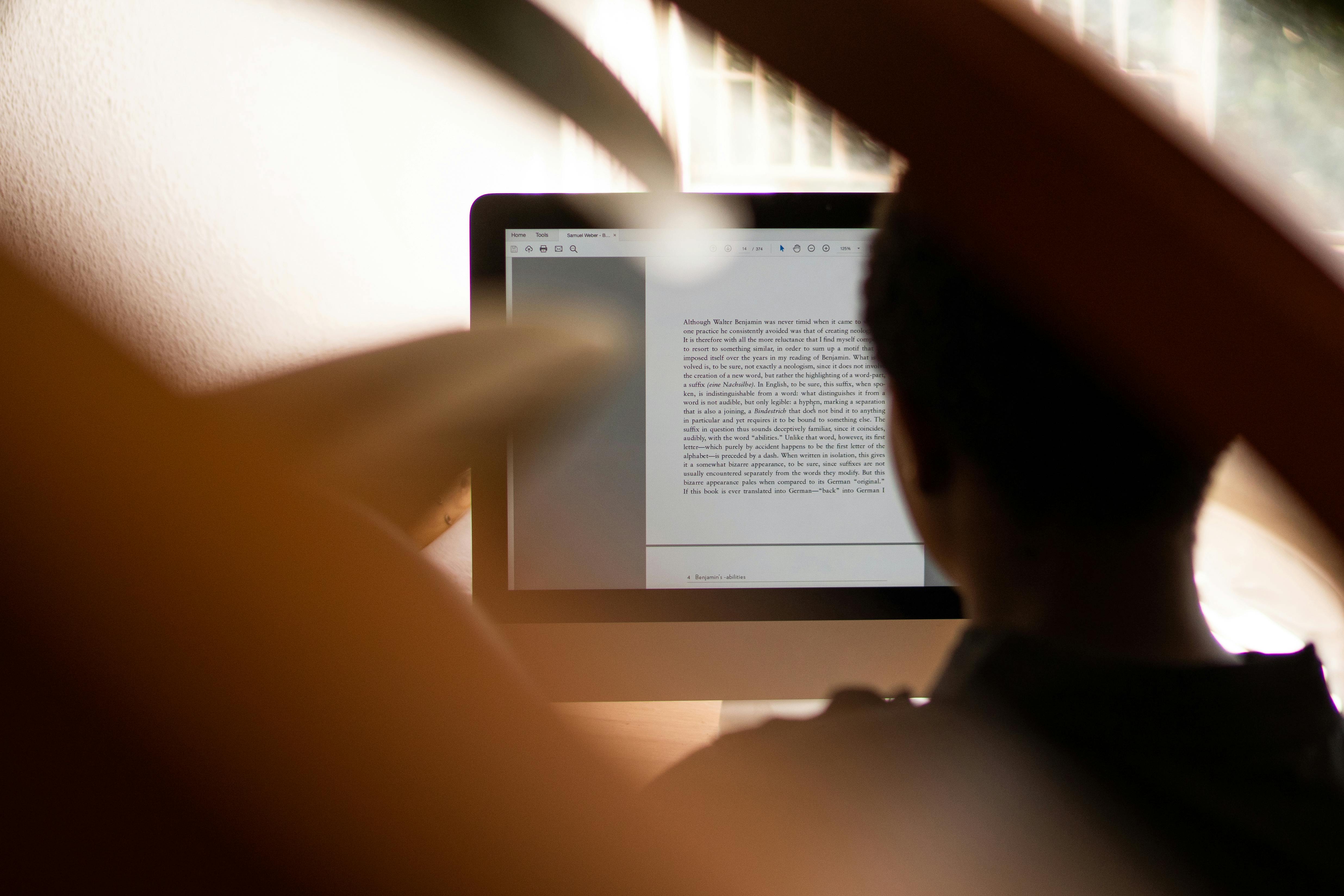 A person reading an e-book on a tablet, viewed from behind, with warm natural lighting in a cozy indoor setting.