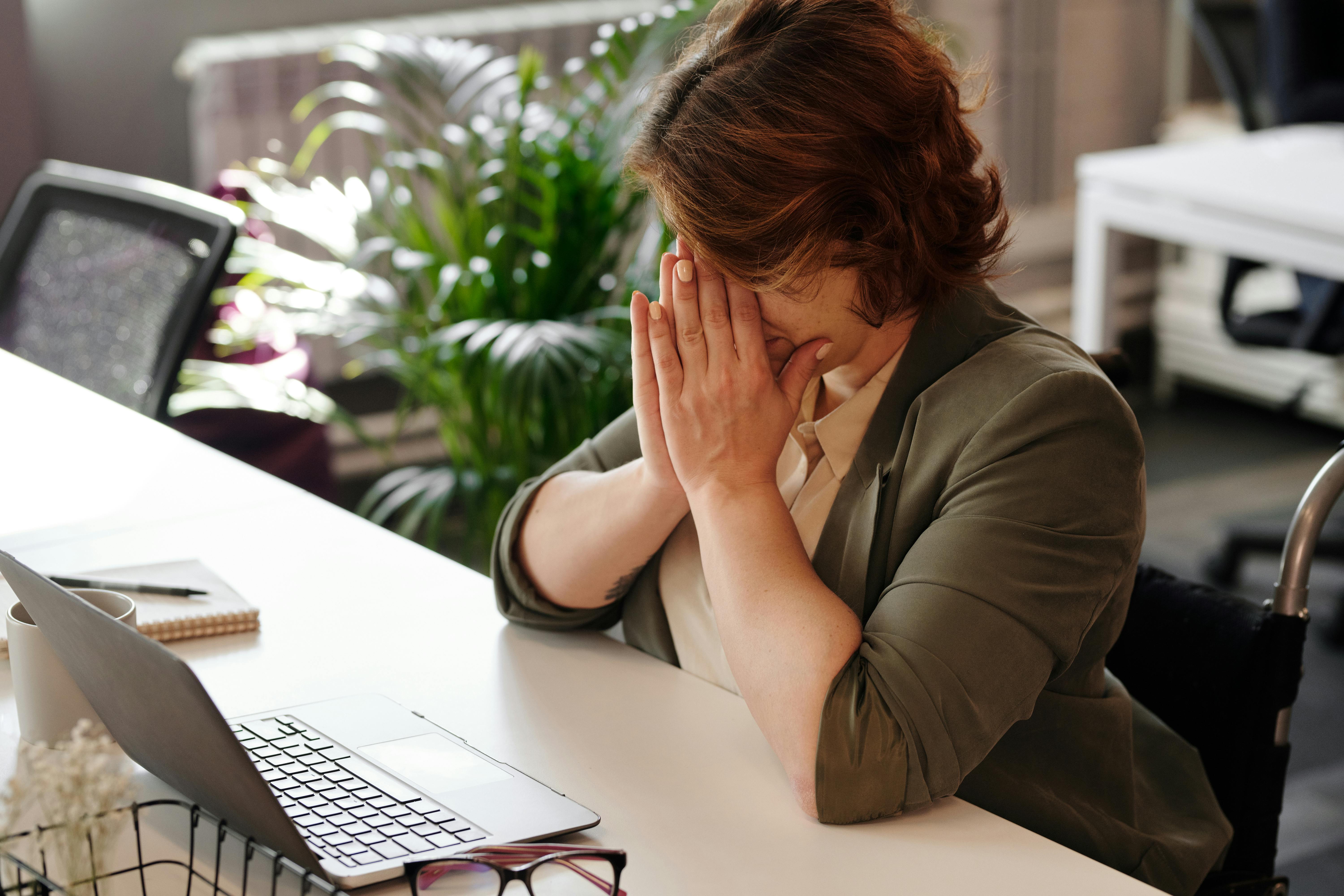 A woman sits at a desk, resting her face in her hands, reflecting on a serious topic related to employee death.