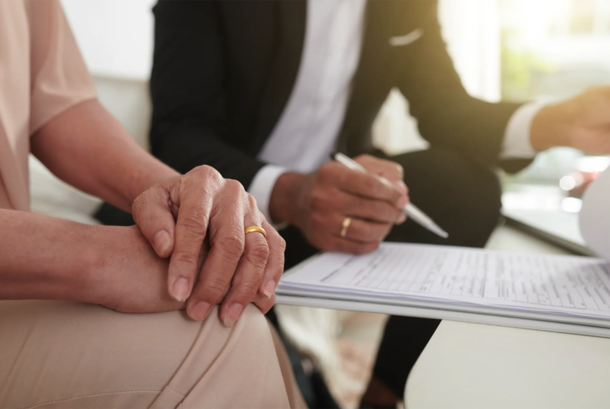 Person resting a hand on another's while a man in a suit writes on a form