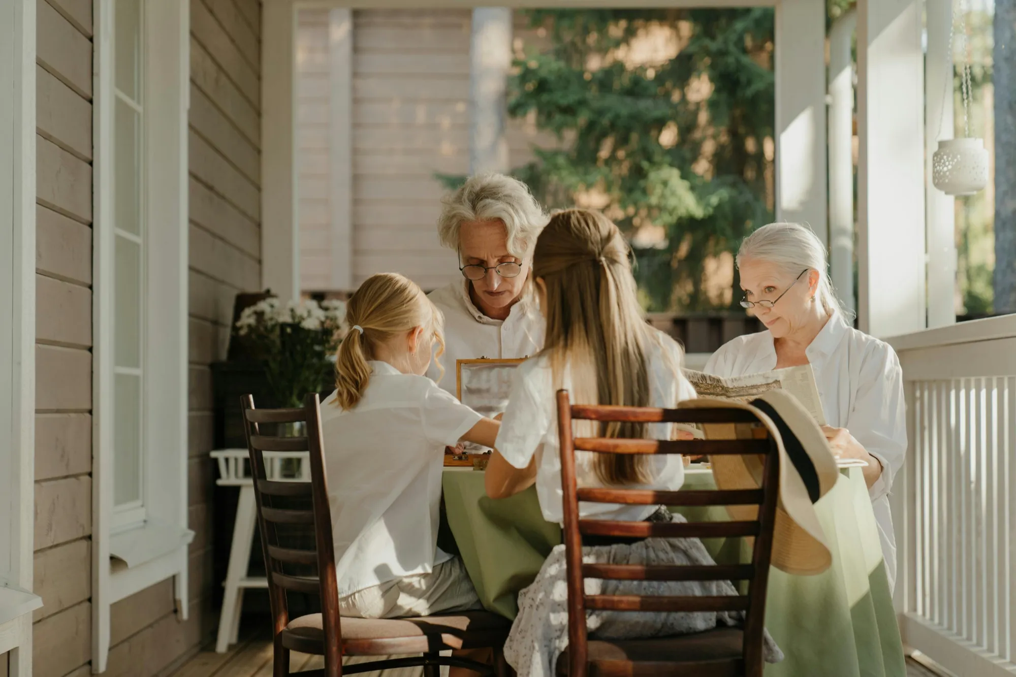 A family of four sits at a table on a sunlit porch, engaged in conversation. The setting is warm and cozy, evoking a sense of togetherness and calm.