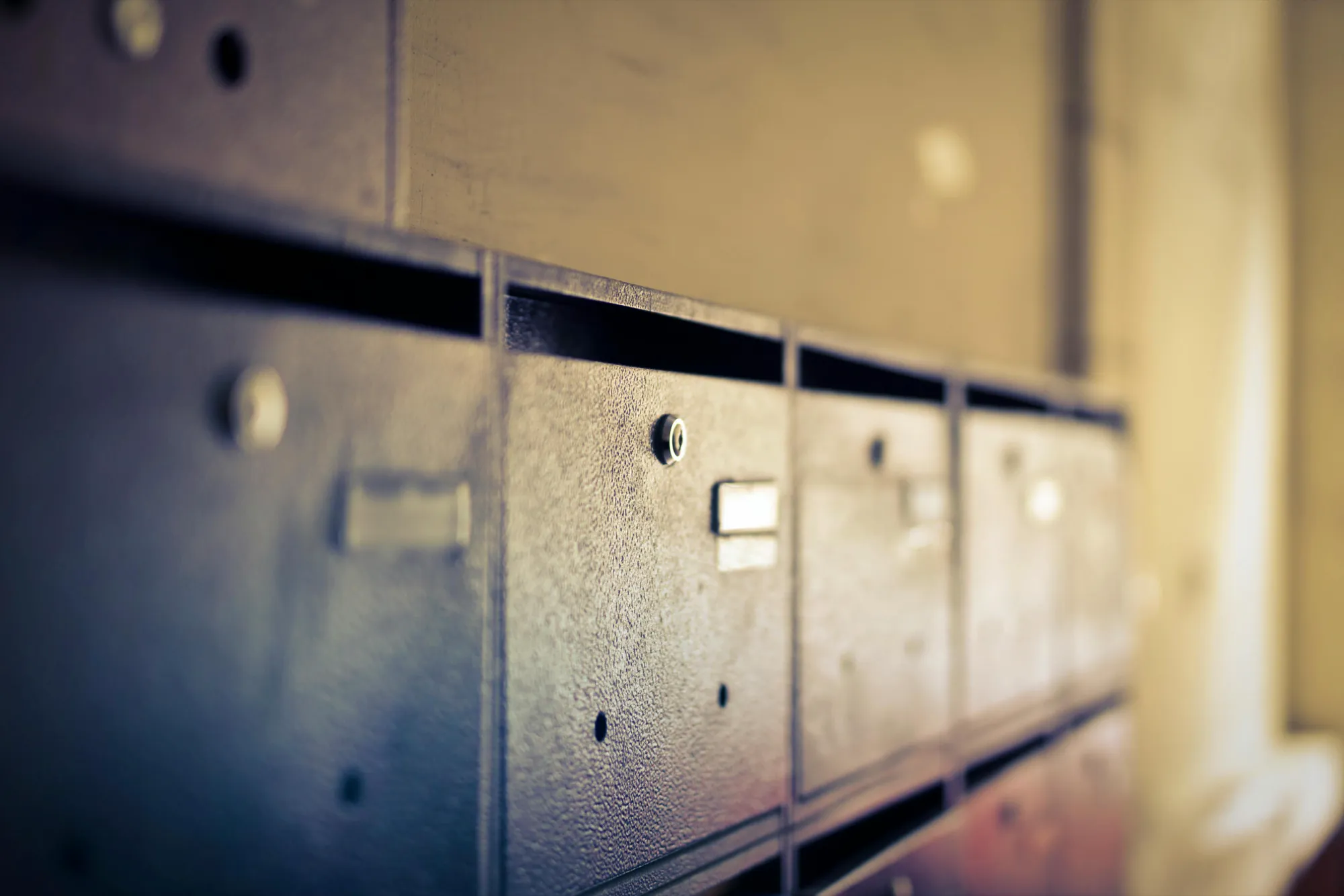 Close-up of vintage-style metal mailboxes in soft focus, creating a nostalgic and tranquil atmosphere with warm lighting and subtle shadows.