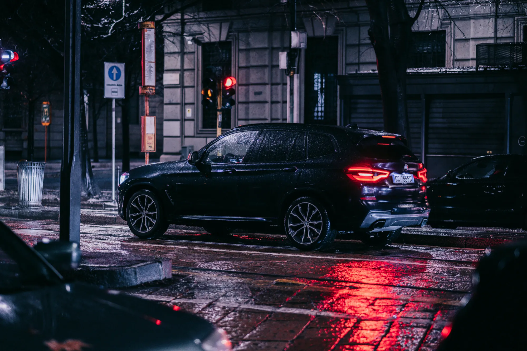 Black BMW X5 parked on a street at night, illuminated by streetlights, with a dark urban backdrop.