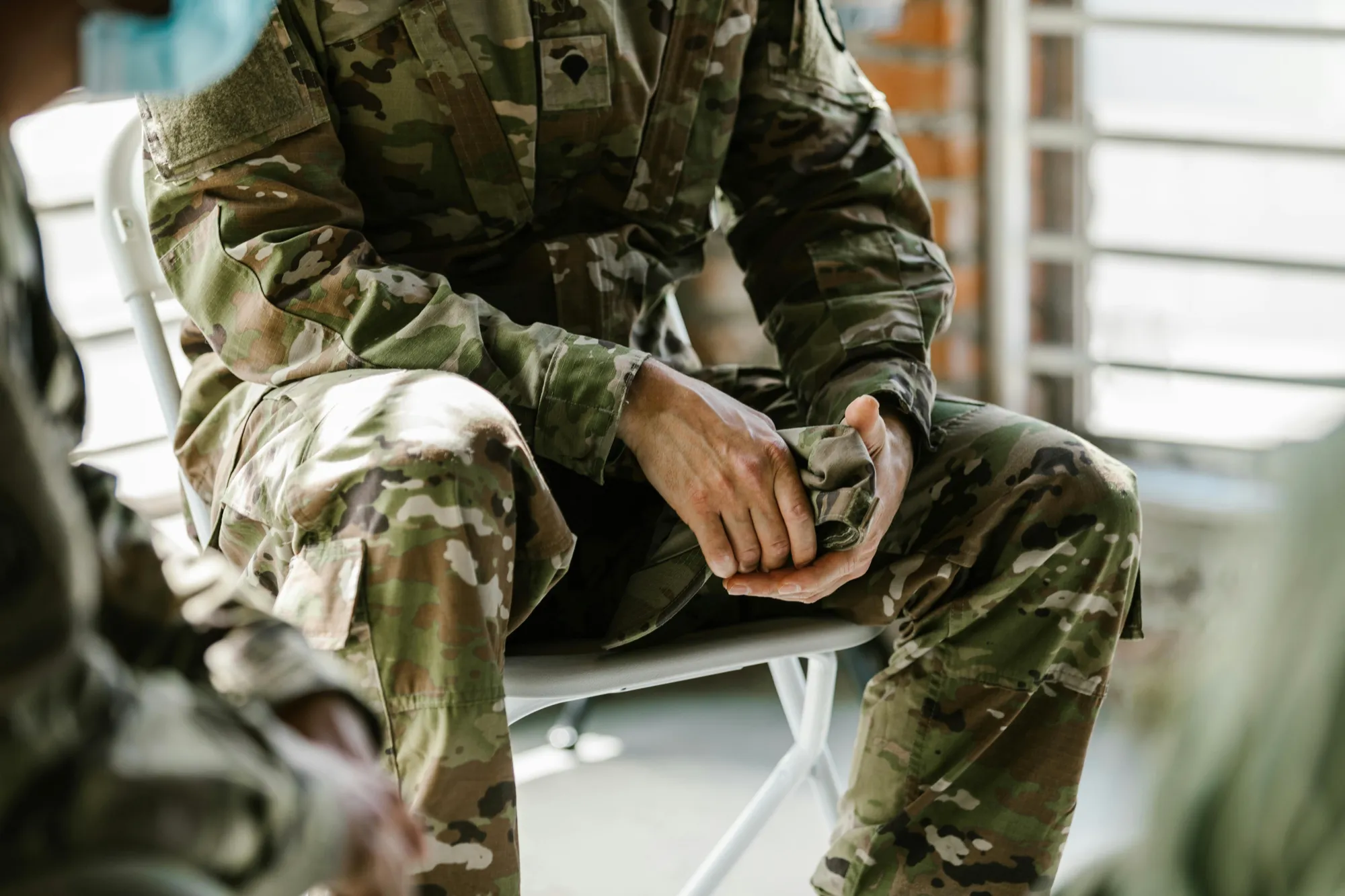 A soldier in camouflage sits on a chair, reflecting on the importance of timely reporting a veteran's death to the VA.