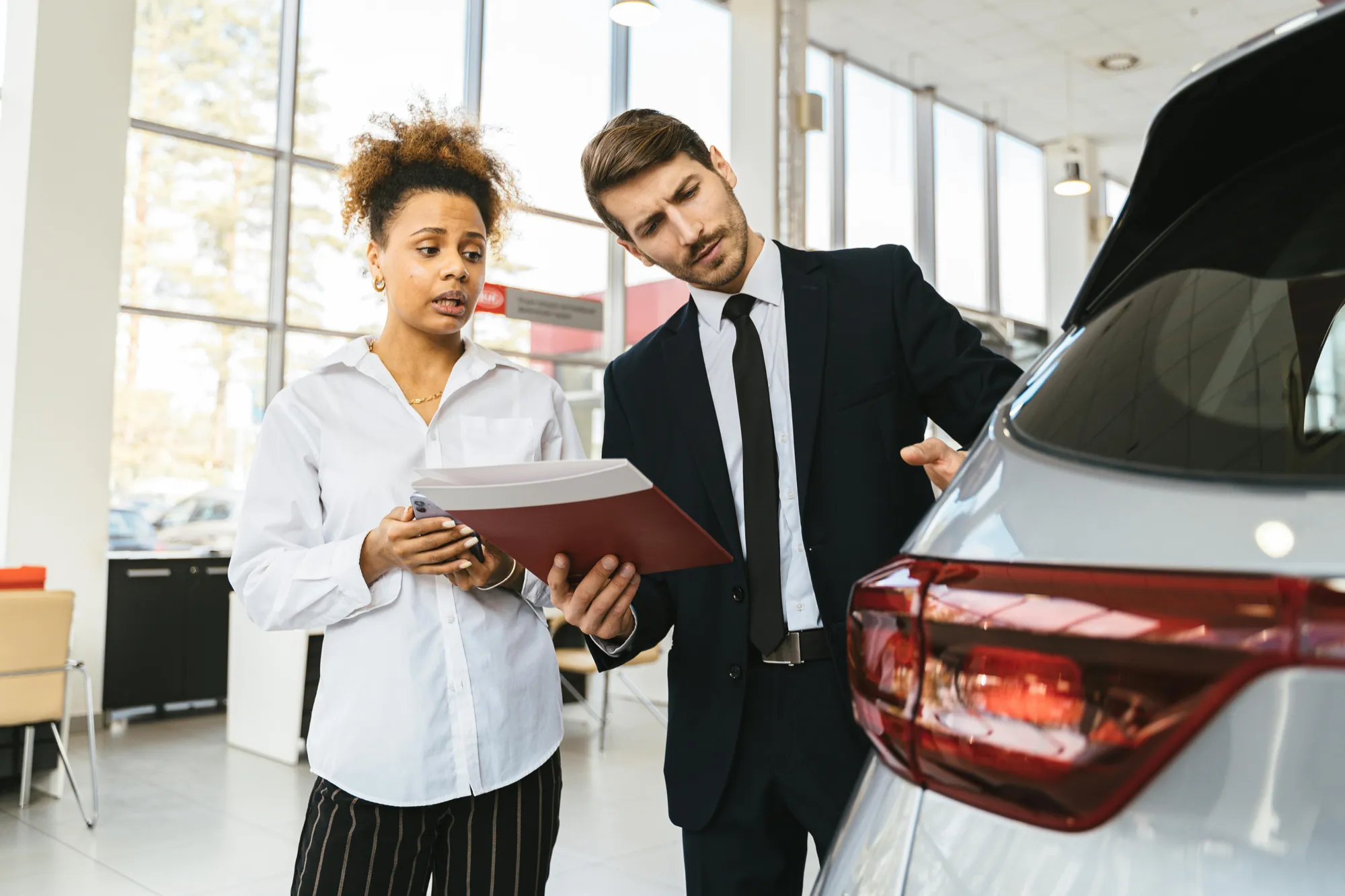 A man and woman at a car dealership reviewing paperwork related to transferring a car title after the owner's death.
