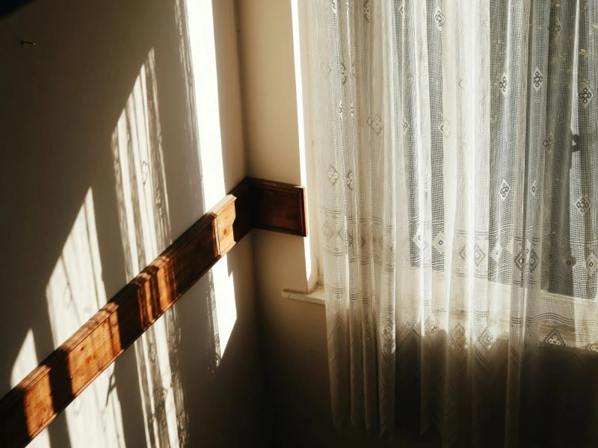 A window with a curtain and wooden railing, symbolizing a peaceful home environment during difficult times.