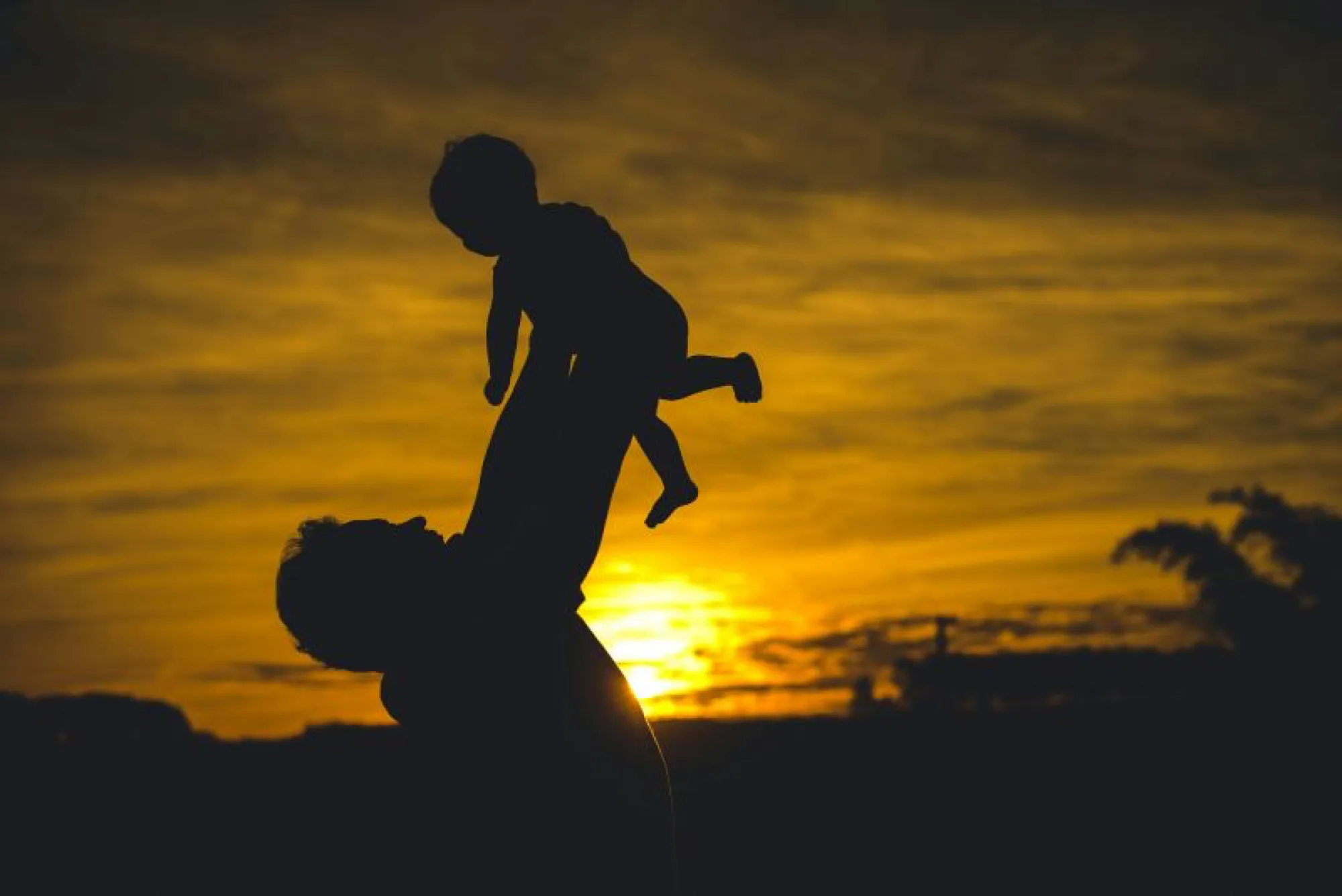 Silhouette of a man lifting a child against a vibrant sunset, symbolizing love and cherished memories.