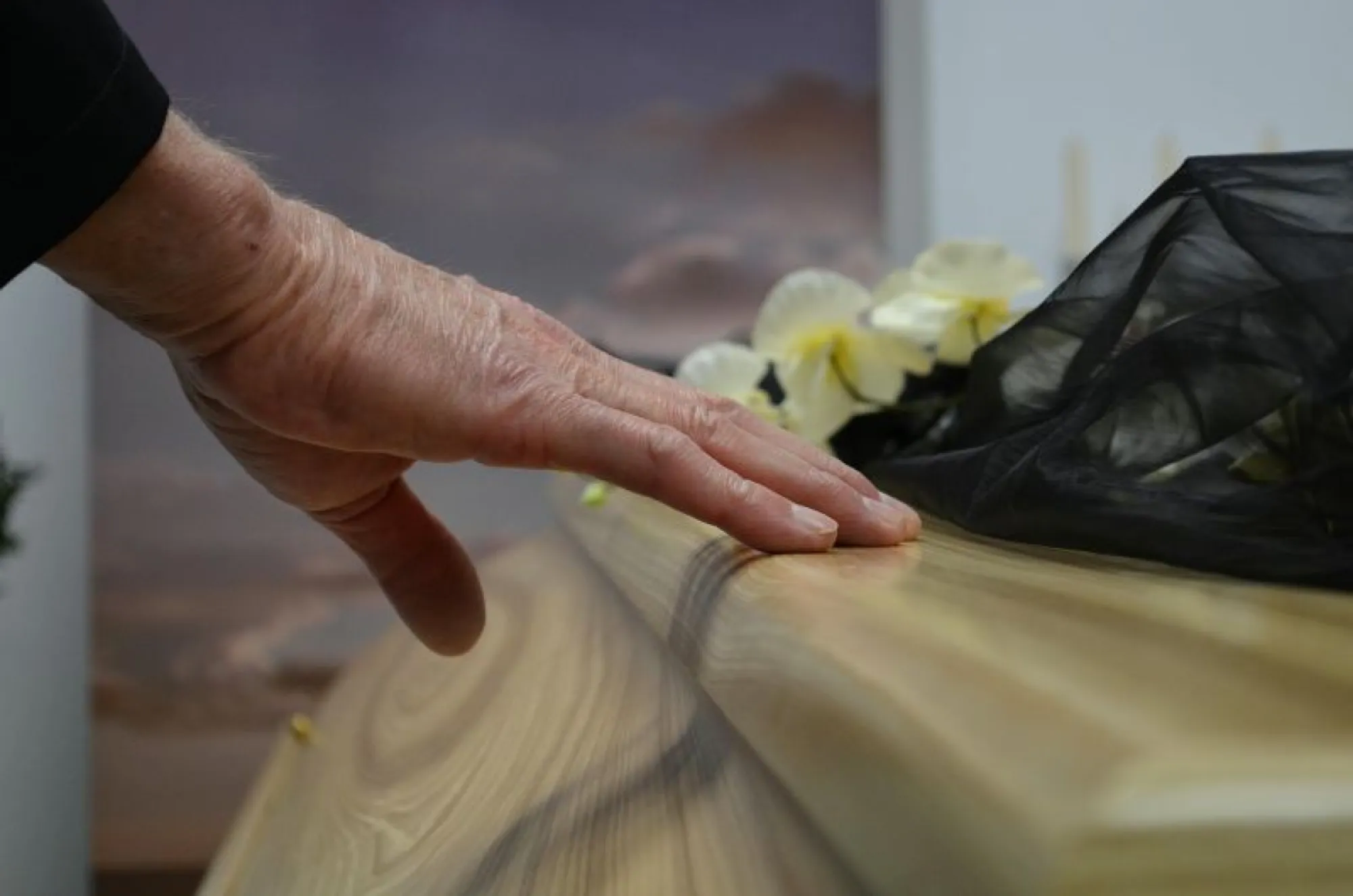 A hand gently touches a casket adorned with flowers, symbolizing remembrance and the importance of thoughtful choices.