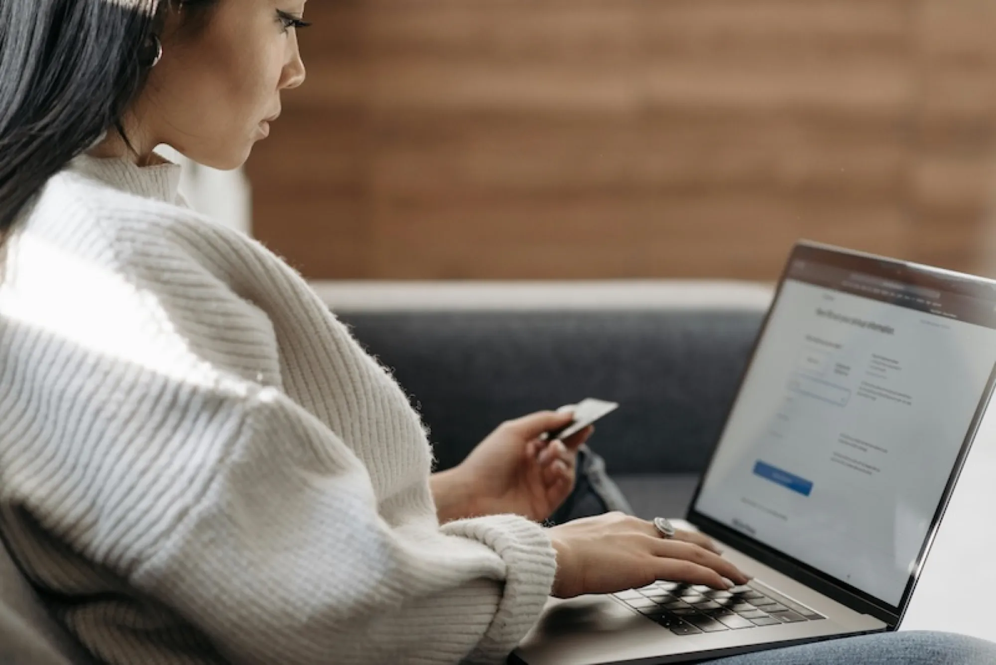 A woman sitting on a couch, focused on her laptop, contemplating credit card debt responsibilities after a loved one's death.