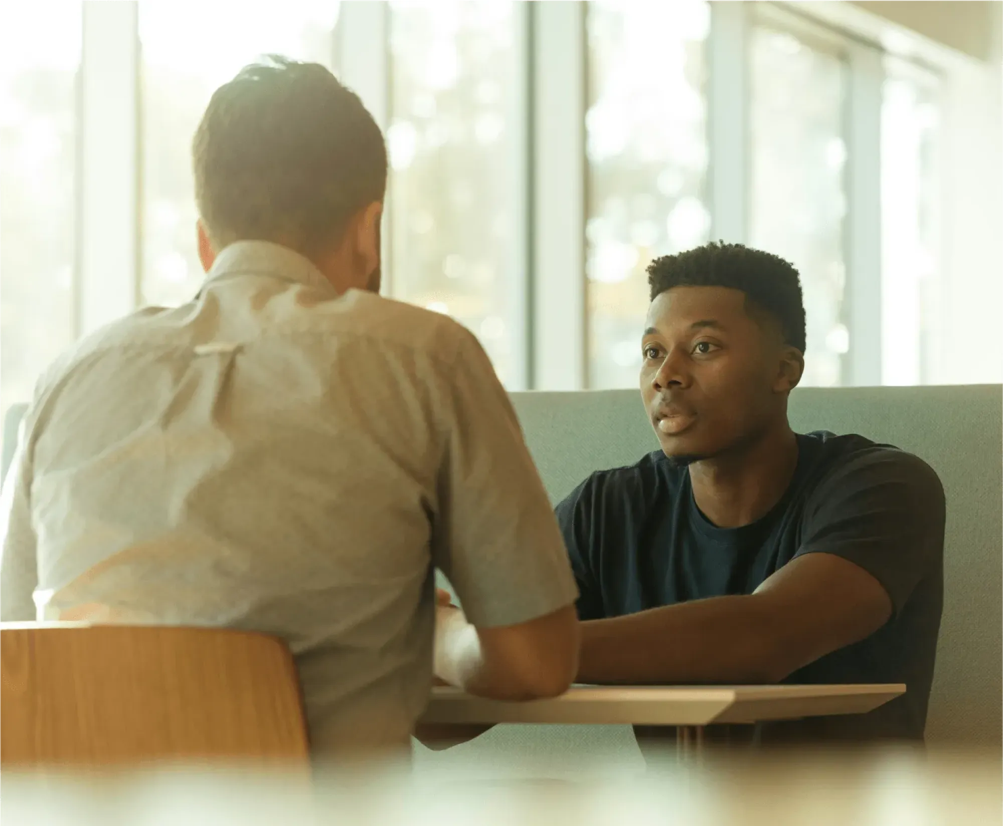 A man at a table engages in conversation with another man, discussing grief in the workplace.